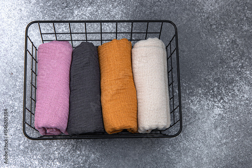 Colorful rolled fabrics neatly arranged in a wire basket on a textured surface