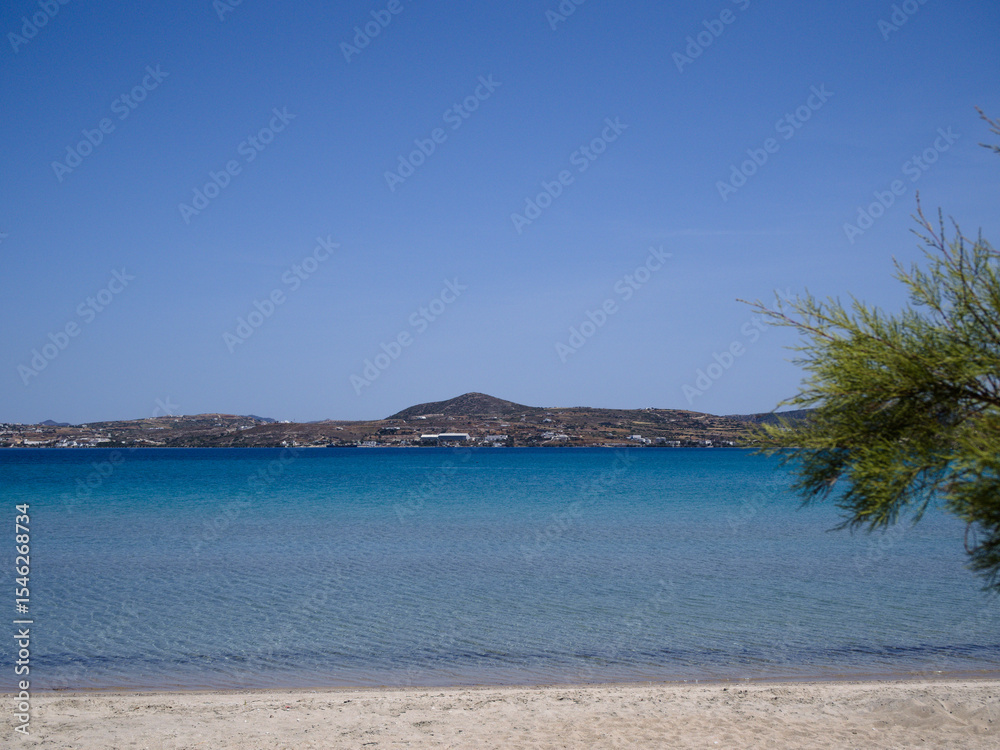 Fototapeta premium Tranquil Achivadolimni Beach on Milos island, Greece, with soft sand, turquoise sea, distant coast and Mediterranean tree under sunny sky.