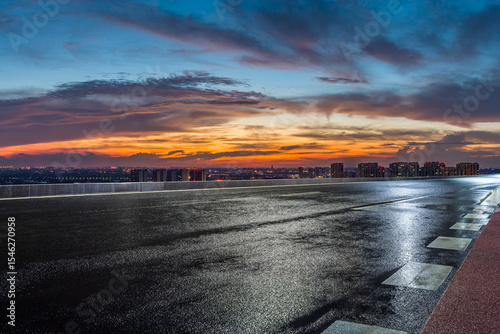 Wet asphalt road and city skyline with beautiful sky clouds at night