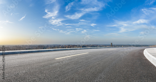 Empty asphalt highway road and city skyline with residential area buildings under blue sky
