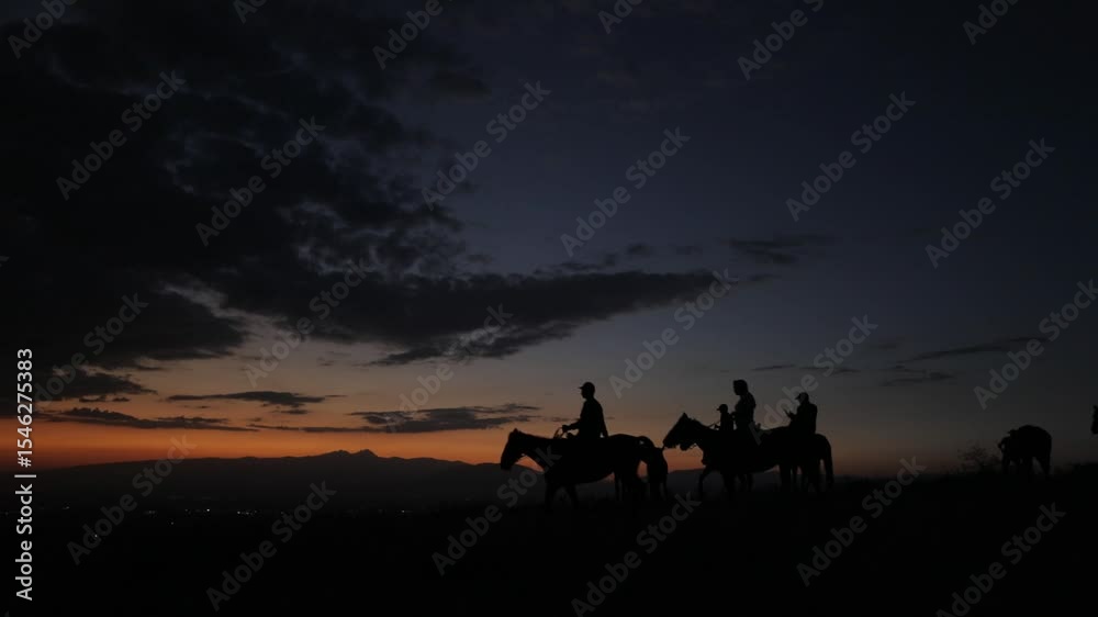 Silhouetted group of people riding horses across a hill against a vibrant sunset sky. Distant mountains and city lights add depth. Evokes freedom, adventure, and natural beauty. Perfect for travel and Silhouetted group of people riding horses across a hill against a vibrant sunset sky. Distant mountains and city lights add depth. Evokes freedom, adventure, and natural beauty. Perfect for travel and