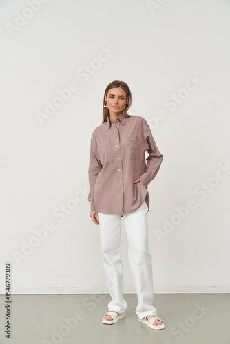 Woman stands confidently wearing a relaxed mauve shirt and white pants, hand in pocket. She pairs her outfit with white slide sandals. Her hair is styled straight, completing the chic look