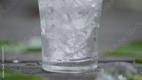 スーパースロー映像：夏の自然の中で、氷が入ったガラスのコップに炭酸水を注ぐ様子