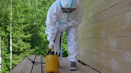 Worker in Protective Suit Spraying Wooden Wall For Pest Control. Safety, disinfection