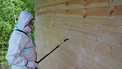 Worker in Protective Suit Spraying Wooden Wall For Pest Control. Safety, disinfection