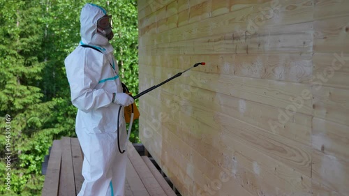Worker in Protective Suit Spraying Wooden Wall For Pest Control. Safety, disinfection