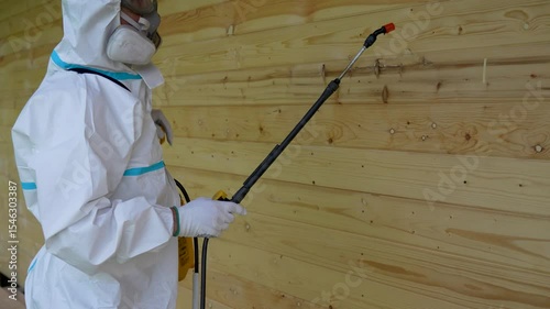 Worker in Protective Suit Spraying Wooden Wall For Pest Control. Safety, disinfection
