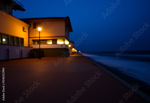 Nighttime coastal boardwalk scene with illuminated buildings and ocean waves