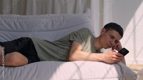 Man scrolling smartphone on sofa at home, concept of phone addiction and social media dependence