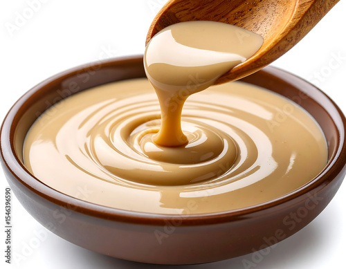 Tahini vegan cream pouring from wooden spoon into brown bowl