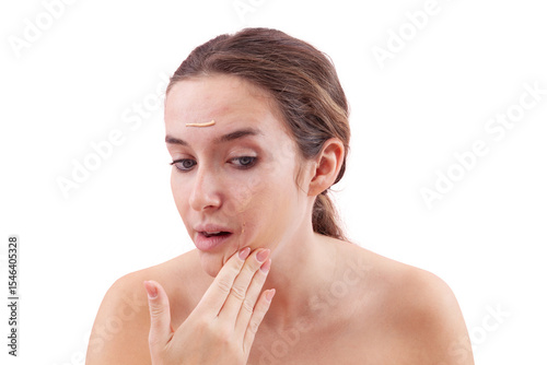 Young woman with natural skin applying foundation cream on face. Visible makeup strokes. Beauty closeup portrait, isolated on white background. Skincare and cosmetics routine, natural look concept.