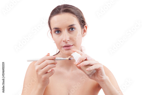 Young woman with natural skin holding foundation pump bottle, dispensing product directly onto makeup brush. Skincare and beauty routine concept. Isolated on white background, clean and minimal look.