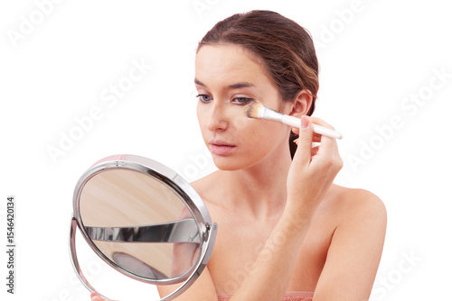 Young woman with natural skin applying foundation with makeup brush while looking into a mirror. Visible foundation streak texture on cheek. Clean beauty routine concept, isolated on white background