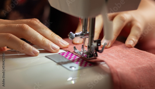 A woman sews on a sewing machine. Hands of a craftswoman. Overlock on fabric. Textile business, tailoring. Hobbies and crafts. Close up photo