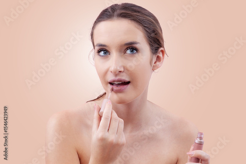 Young woman applying lipstick on her lips with a lip brush applicator as part of her makeup routine. Beauty concept with a fresh, natural look. Isolated on beige background, clean and minimal