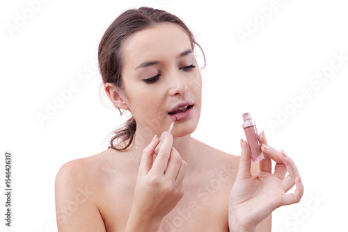 Young woman portrait applying lipstick with lip brush applicator holding lipstick bottle near her face and looking at it. Natural skin with smooth foundation. Beauty routine concept. Isolated on white