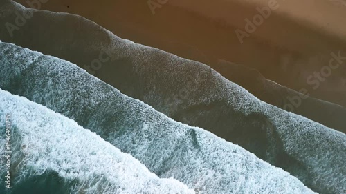 Gentle ocean waves lapping diagonally against a sandy beach
