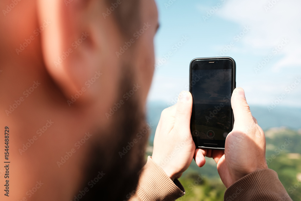 Fototapeta premium Close-up of a phone screen as a man records a scenic mountain view in Serbia on a spring day. Rear close view