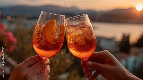 Hands toasting with aperol spritz at sunset overlooking the sea