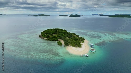 Aerial around view of small tropical island with clear sea waters and lush greenery surrounded by distant islands, Philippines, 4k