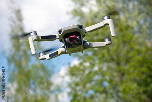 Small Flying Qunmanned aerial vehicle in flight mode with camera outdoor on sunny day summer time blue green garden background