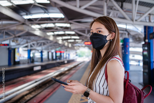 Asian woman is using a smartphone while waiting for the train at the station