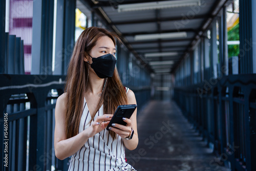 Asian woman using a smartphone while walking on an elevated walkway in the city