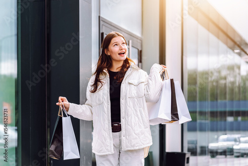Joyful shopper celebrating discounts while carrying bags outside a modern store