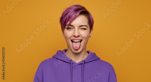 Playful young woman with purple short hair playfully sticking out her tongue against a vibrant yellow background showcasing youthful energy and expressive style.