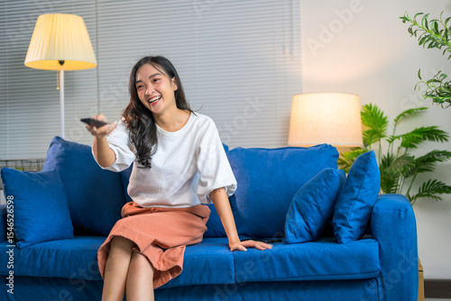 Young woman changing channels while laughing and watching television on blue couch