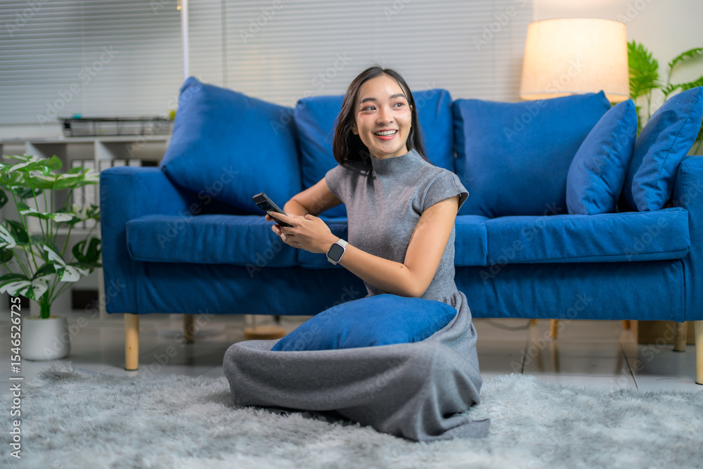 Obraz premium Happy asian woman using mobile phone while sitting on floor in living room