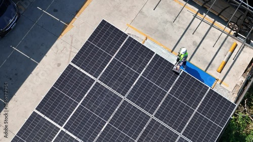 Aerial view of a solar panel installation on a parking structure. A technician in safety gear is inspecting the photovoltaic system. Promoting clean energy and sustainability in urban infrastructure.