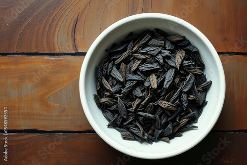 White bowl filled with dried dark elongated leaves on a woodgrain surface