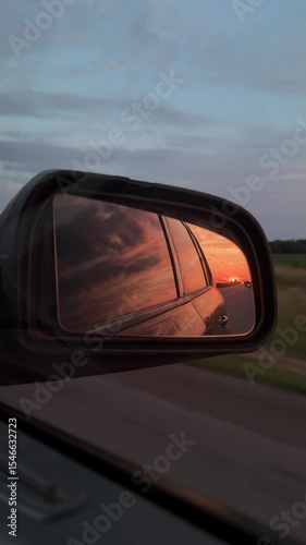 The sun is reflected in the mirror, evening road. View in mirror of a car driving along the highway