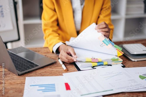 Adult Woman Hands Organizing Financial Documents at Office Desk with Laptop Charts and Calculator for Business Report Analysis