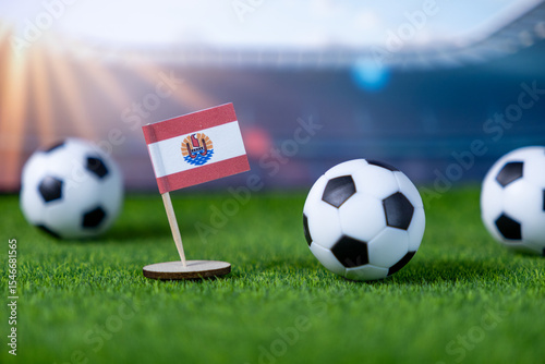 French Polynesia flag miniature stands on green grass with soccer balls and stadium in background, symbolizing the nation's team in global sports
