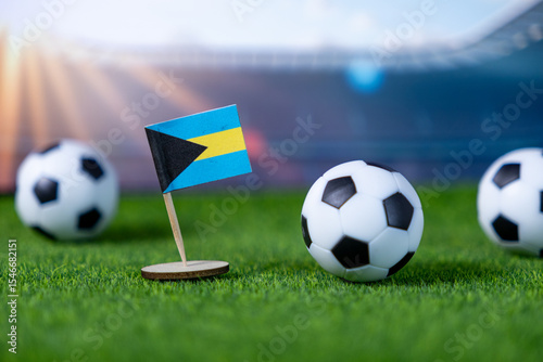 Bahamian flag mini stands on green artificial grass with soccer balls, symbolizing the nation's team pride in international football competitions