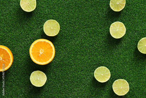 Orange and lime halves on grass background, top view. Summer background. Oranges and limes on artificial grass. Citrus fruits. Summer composition. Products with vitamin C. Bright fruit background