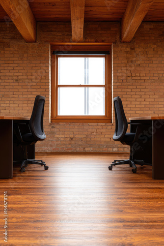 Two office chairs are facing each other in front of a window in a room with brick walls and wooden flooring. Empty office space concept