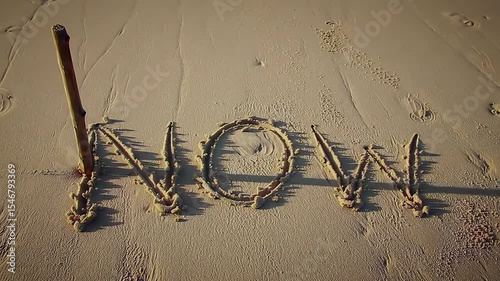 Beach sand, stick, word NOW written, time, ephemerality, nature, transient moment, sun, shadow, wave, erosion
