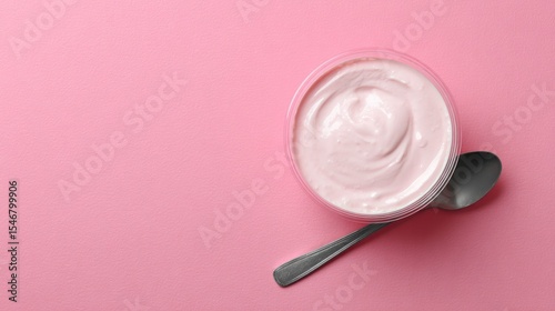 Pink background showcasing yogurt in a plastic cup with spoon, top view with space for text