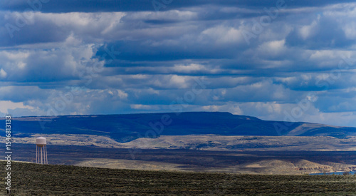 Thick clouds over mountains near lake, water tower on horizon in mountains in Utah