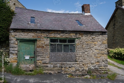 Tablou pe pânză Rustic stone cottage with boarded windows and sagging roofline a weathered green painted door