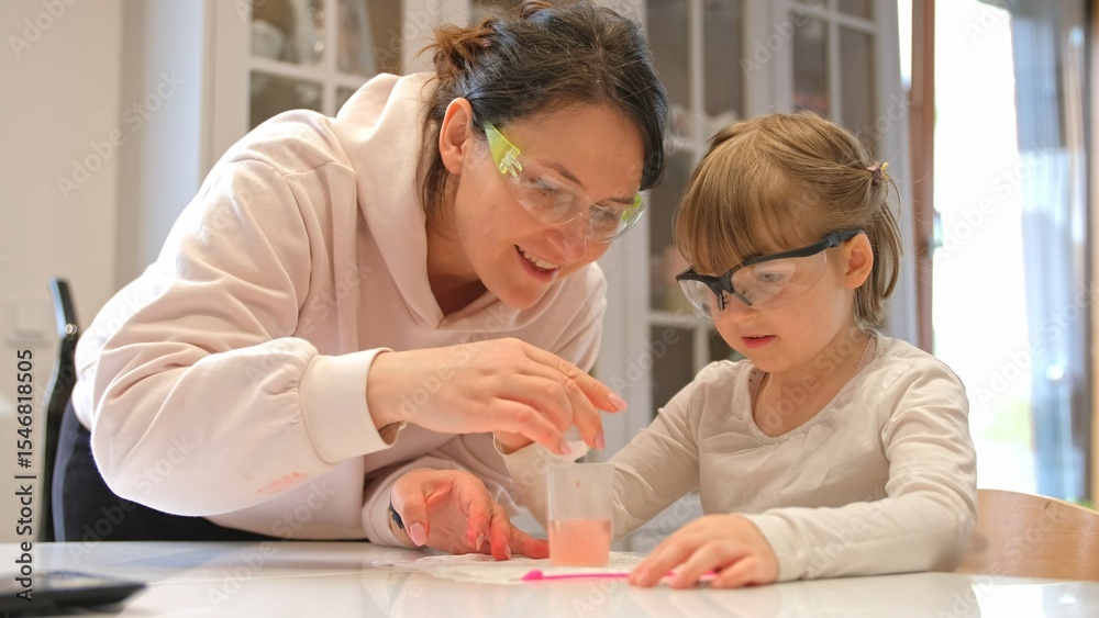 Fototapeta premium Caucasian Woman and Preschooler Daughter Child Girl Wearing Protective Glasses Having Fun Preparing STEM Science Experiment on Kitchen Table using Education Kit for Homeshooling Learning