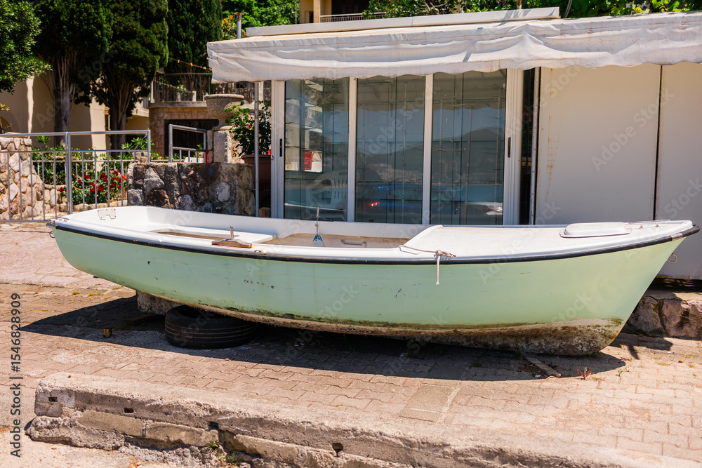 Obraz premium Old boat on asphalt near shop. Coastal lifestyle, fishing culture, and marine equipment storage