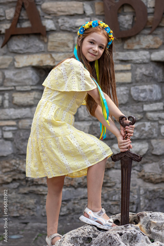 Young girl smiling while holding a sword outdoors in front of a stone wall