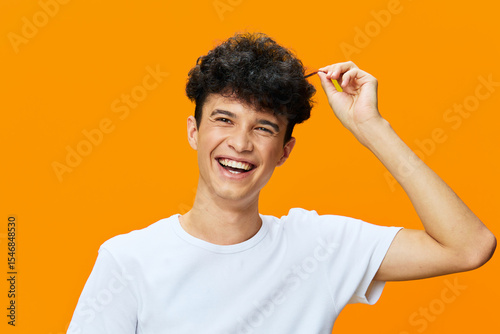 smiling young man with curly hair wearing white t-shirt on vibrant orange background, happy expression, casual style, bright color contrast