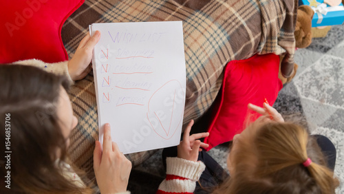 Cute little girl with mom writing making checklist sitting on floor in decorated living room