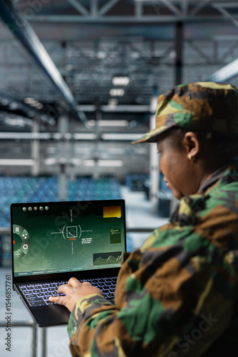 Close up of army expert in data center scanning terrain in real time using military satellite control. Military units wearing uniform in server farm managing orbital telemetry on laptop
