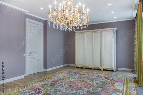 Exquisite interior of the room in a classic style. A luxurious chandelier over 
a patterned carpet, a cabinet with carvings and gilding, a beautiful drapery on the window.